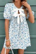 Woman wearing a blue floral dress with a white bow tie against a green background