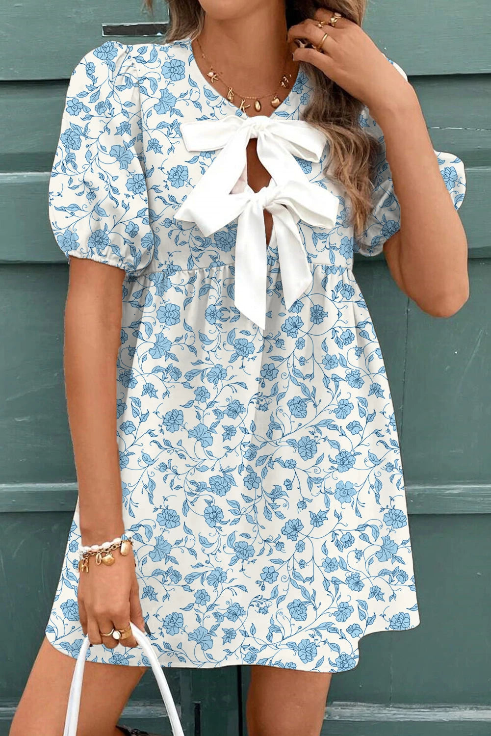 Woman wearing a blue floral dress with a white bow tie against a green background